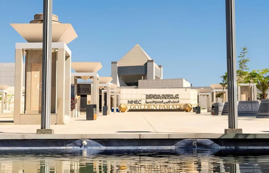 The modern entrance of the National Museum of Egyptian Civilization (NMEC) building with a water feature and clear blue sky.