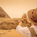 Tourist wearing a sun hat photographs the Sphinx and the Great Pyramids of Giza during an exciting 3 Day Tour in Cairo.