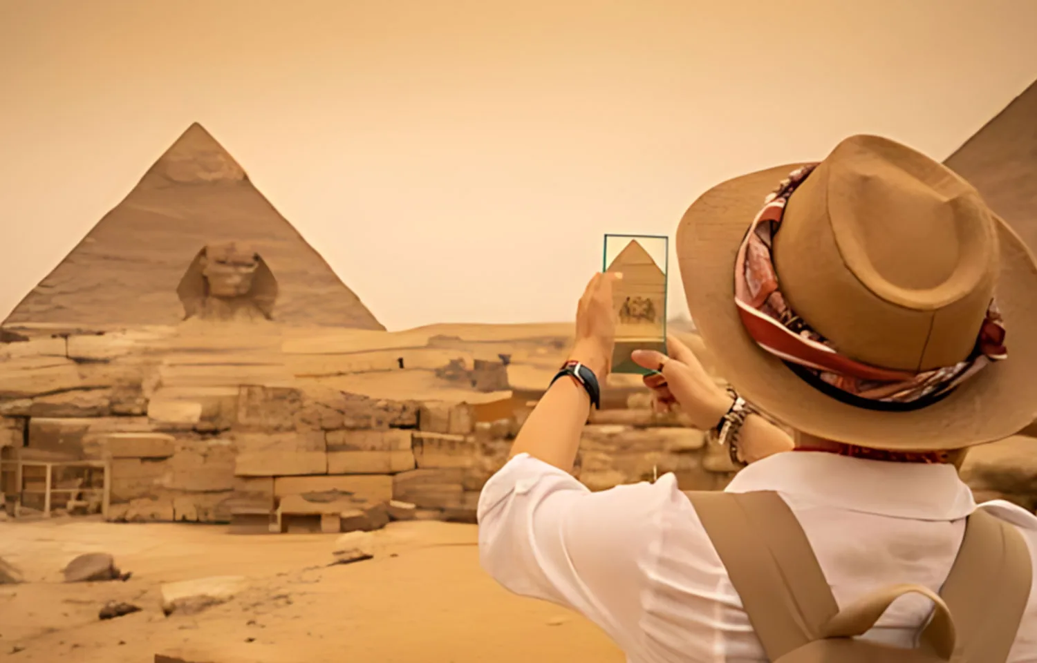 Tourist wearing a sun hat photographs the Sphinx and the Great Pyramids of Giza during an exciting 3 Day Tour in Cairo.
