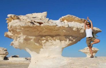A female traveler doing a yoga tree pose next to a unique white chalk rock formation in the White Desert during a 9 day highlights of Egypt adventure tour