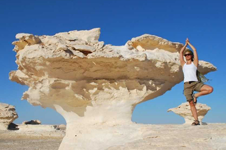 A female traveler doing a yoga tree pose next to a unique white chalk rock formation in the White Desert during a 9 day highlights of Egypt adventure tour
