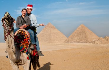 A couple riding a camel in front of the Giza Pyramids during a 9-day Christmas overland Egypt holiday.