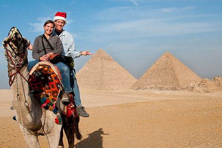 A couple riding a camel in front of the Giza Pyramids during a 9-day Christmas overland Egypt holiday.