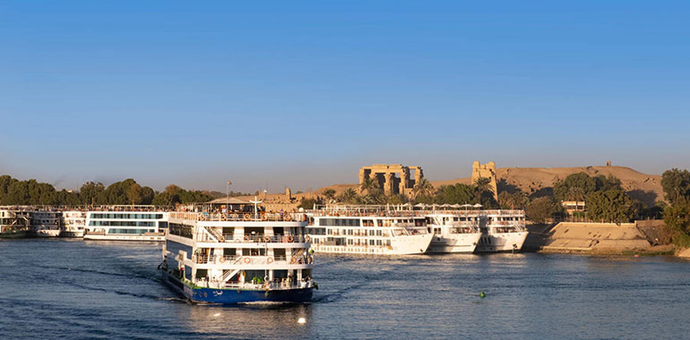 A Nile Cruise On River With Ruins Of Kom Ombo On Nile Riverbank