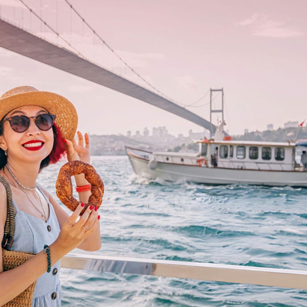 A Tourist enjoys a fresh simit by the Bosphorus in Istanbul savoring the traditional sesame covered snack on a summer day