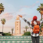 A-Young-woman-celebrating-reaching-Koutoubia-Mosque-in-Marrakech-with-open-arms-enjoying-her-trip-to-Morocco