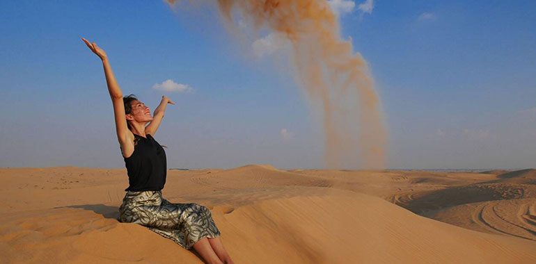 A Girl In The Dubai Desert Throws Sand Up And Smiles