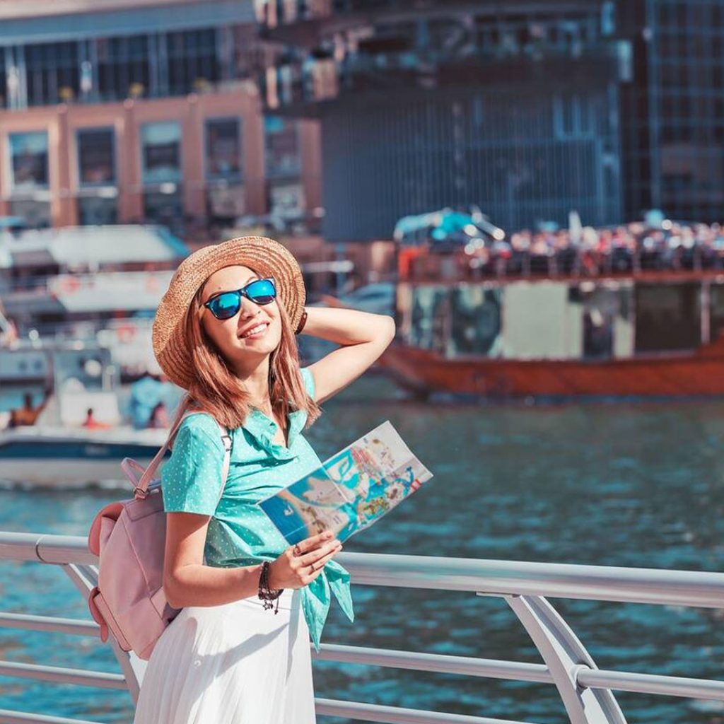 A Happy Traveller Girl With A Map Is Waiting For Her Cruise Ship At The Marina Port In Dubai