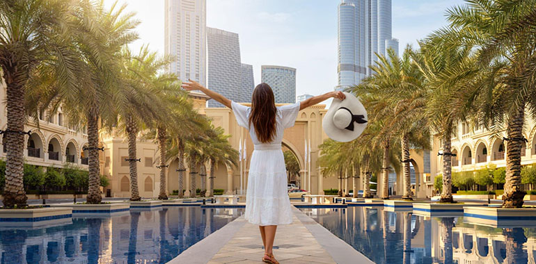 A tourist woman stands on a public square with palm trees at Downtown Dubai