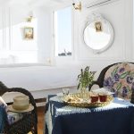A cozy seating area in a Nile cruise cabin with wicker chairs, a blue draped table, and large windows overlooking the river.