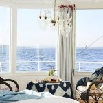 Sunlit cabin interior of a Nile cruise boat featuring wicker chairs and a large bay window overlooking the river.
