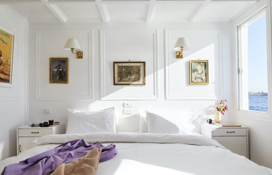 A bright, elegant white cabin on a Nile cruise ship featuring a large bed with a view of the river.