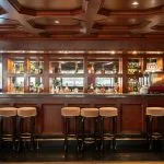 Elevated view of the rectangular swimming pool and six green-striped sun loungers on the top deck of the Nile Admiral cruise ship, facing the Nile River and green riverbanks.