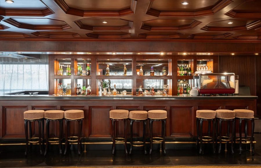 Elevated view of the rectangular swimming pool and six green-striped sun loungers on the top deck of the Nile Admiral cruise ship, facing the Nile River and green riverbanks.