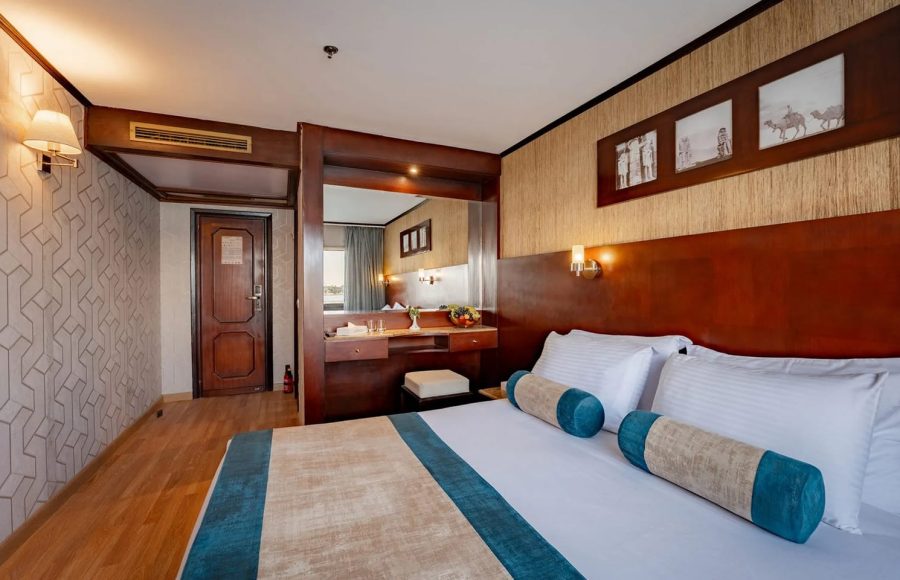 View of the queen bed and vanity mirror area in a comfortable, wood-accented cabin on the Nile Admiral cruise ship.