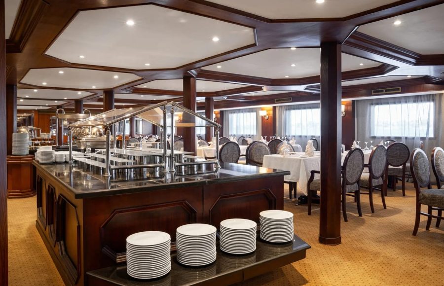 Buffet counter with a black marble top and stacked white plates in the elegant dining room of the Nile Admiral cruise ship.