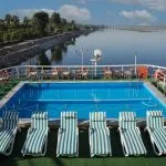 Swimming pool and sun loungers on the upper deck of the Nile Admiral cruise ship, offering a panoramic view of the Nile River and palm-lined banks.