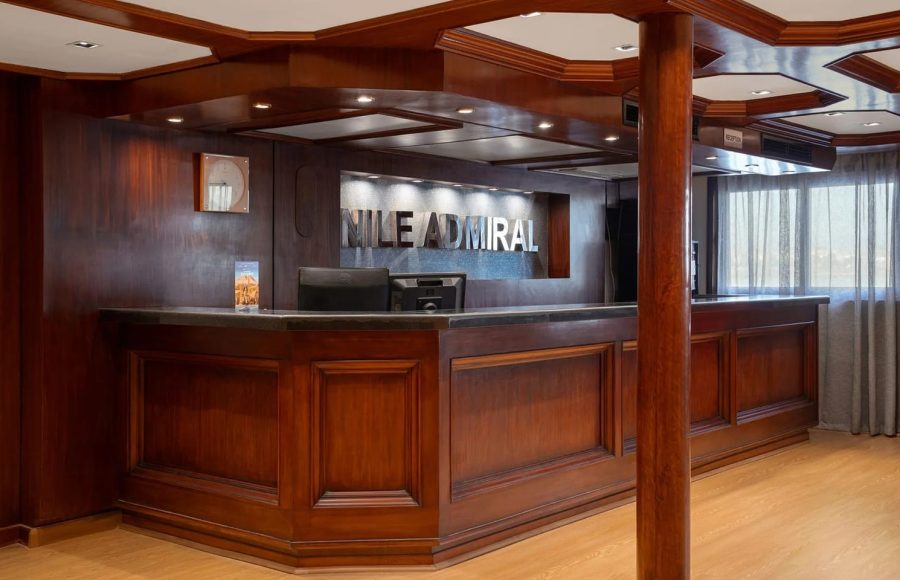 The elegant, dark wood reception desk of the Nile Admiral cruise ship lobby with the ship's name prominently displayed on the back wall.