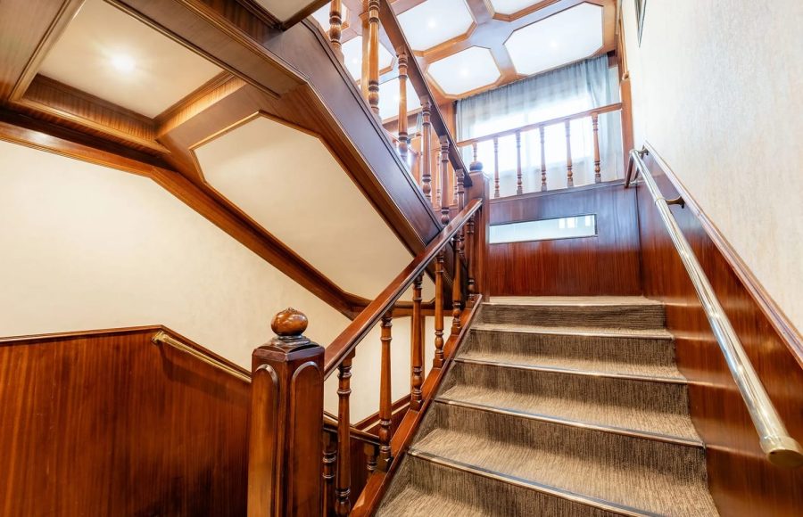Interior staircase of the Nile Admiral cruise ship featuring polished dark wood banisters and balusters, and carpeted steps.