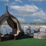 Sun deck of the Nile Admiral cruise ship with a wicker cabana and round sun lounger, overlooking the Nile River under a blue sky.