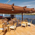 Wooden outdoor dining area on a boat deck under a pergola