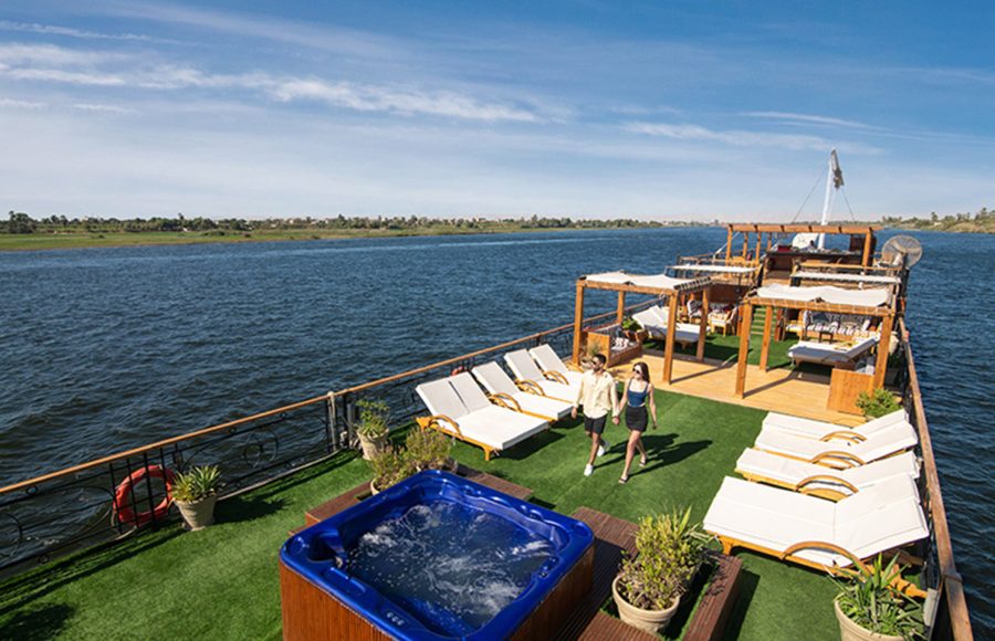 Couple walking on a green turf sundeck with a blue jacuzzi.