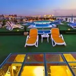 The outdoor sun deck of the Al-Hambra Nile Cruise at dusk, featuring green artificial turf, yellow and white lounge chairs, a small swimming pool, and glass skylights looking into the lower decks.