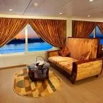 A luxury cruise suite sitting area with a striped couch and glass coffee table in front of large windows overlooking the Nile at dusk.