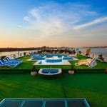 Wide view of a cruise ship sun deck during the day with a pool, green turf, and lounge chairs overlooking the Nile River.