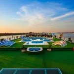 Wide view of a cruise ship sun deck during the day with a pool, green turf, and lounge chairs overlooking the Nile River.