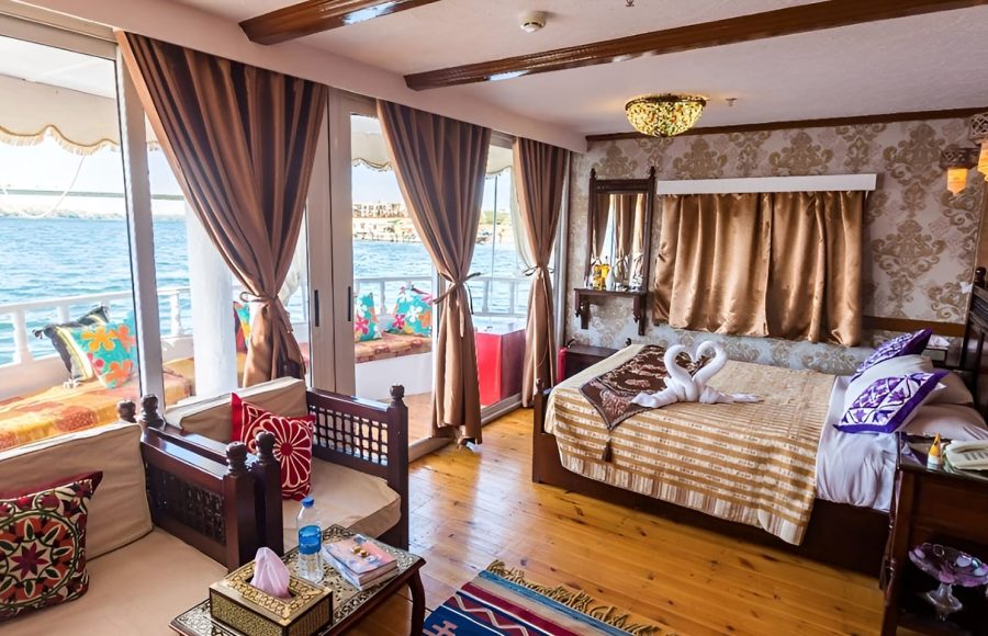 A spacious boat cabin with a double bed, swan-shaped towels, and floor-to-ceiling windows.