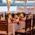 A formal dinner table set with white cloths, candles, and wine glasses at twilight.