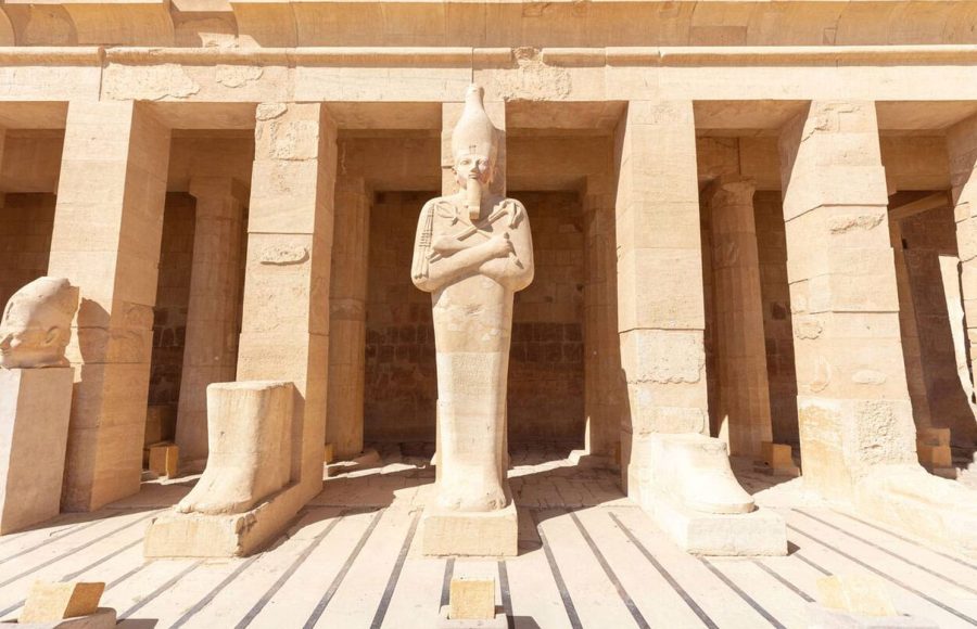 A detailed view of an Ancient place with engraved figure in the Hatshepsut Temple, showing a large, standing Osiris statue of the Queen under the bright sun, a key stop on an Egypt culture trip.