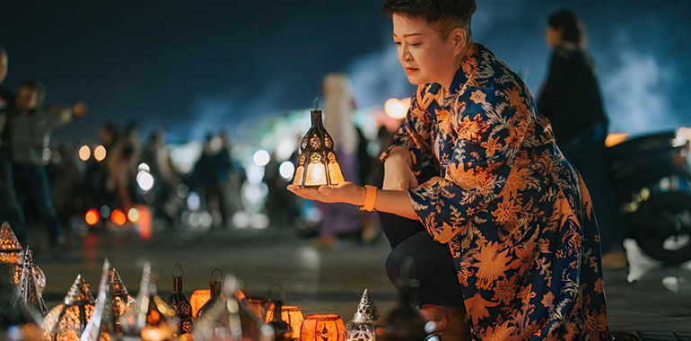 Asian Chinese female tourist choosing lantern at night market stall in Djemma El Fna Marrakech Morocco