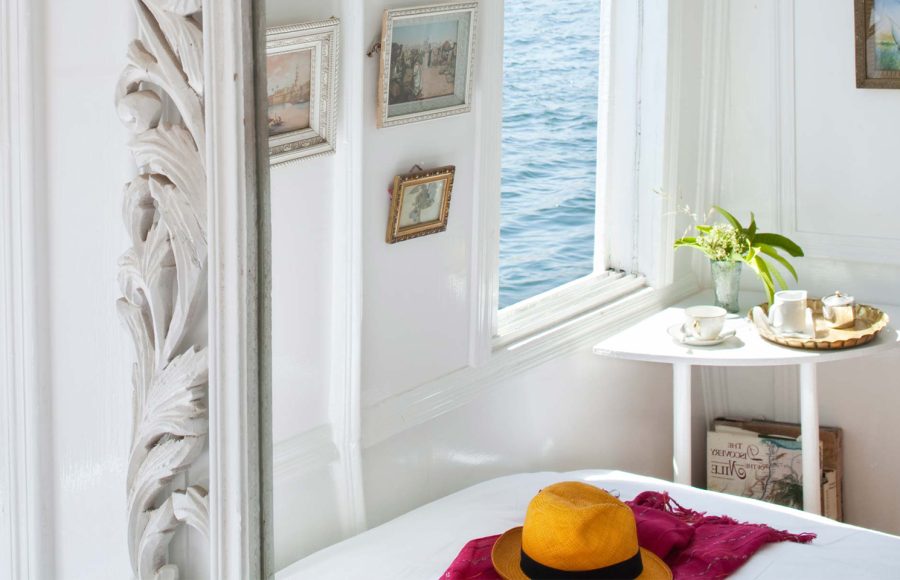 Interior view of a bright white cabin on a Dahabiya Nile cruise boat overlooking the water.