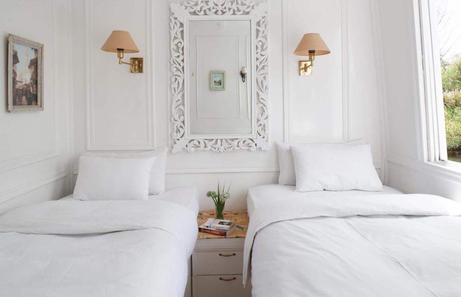 A bright, white twin-bed cabin on a Dahabiya Nile cruise boat with ornate wall molding and a decorative mirror.