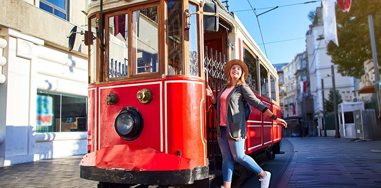 Beautiful young girl tourist in a hat poses in front of tram at popular Istiklal street in Beyoglu Istanbul Turkey