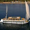 An aerial shot of a traditional white Dahabiya sailing vessel on the blue water of the Nile.