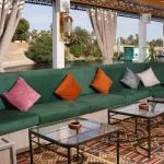 A long, green sectional sofa with colorful throw pillows in a shaded outdoor lounge area.