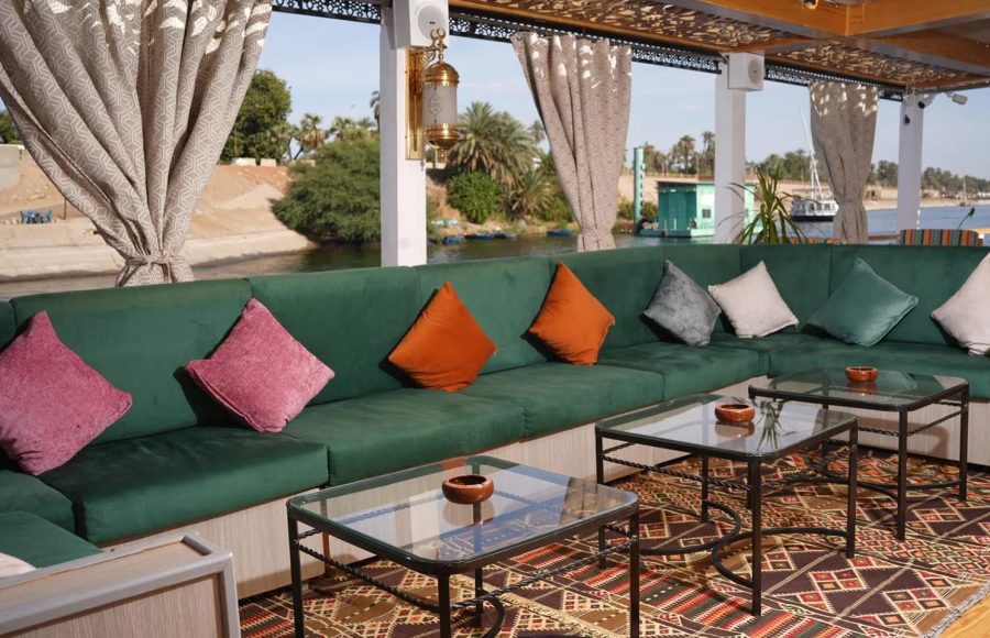 A long, green sectional sofa with colorful throw pillows in a shaded outdoor lounge area.