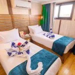 A cruise ship cabin with two twin beds featuring decorative towel art and blue velvet runners.