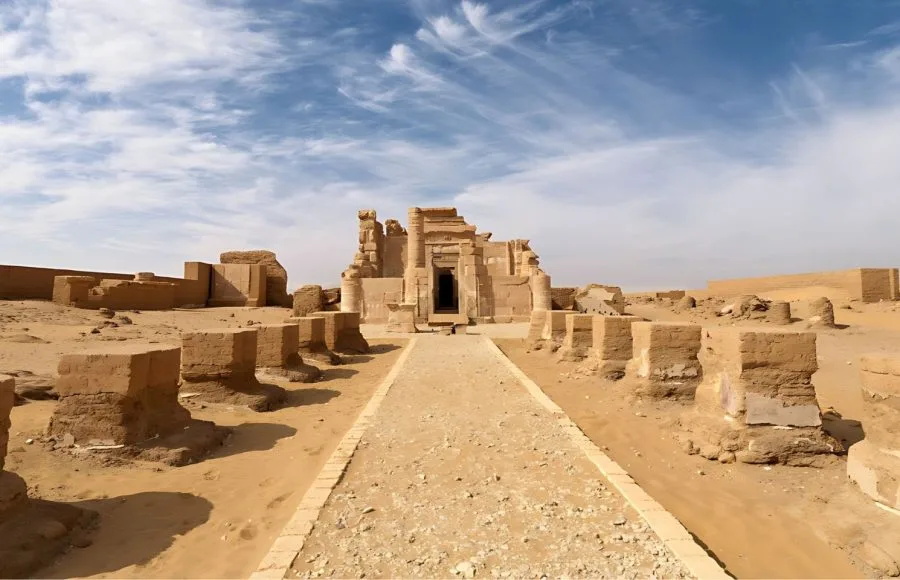 A wide view of the partially ruined Roman Temple Of Deir El Hagar Dakhla Oasis Western Desert Of Egypt, showing the entrance structure and surrounding stone blocks against a striking blue sky.