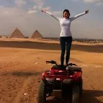 A woman standing on a red ATV during a Cairo quad biking at pyramids tour with Giza in the background