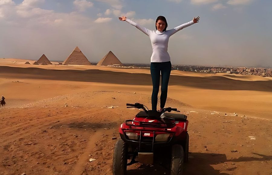 A woman standing on a red ATV during a Cairo quad biking at pyramids tour with Giza in the background
