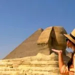 A traveler enjoying a Cairo pyramids half-day tour while posing playfully with the Great Sphinx