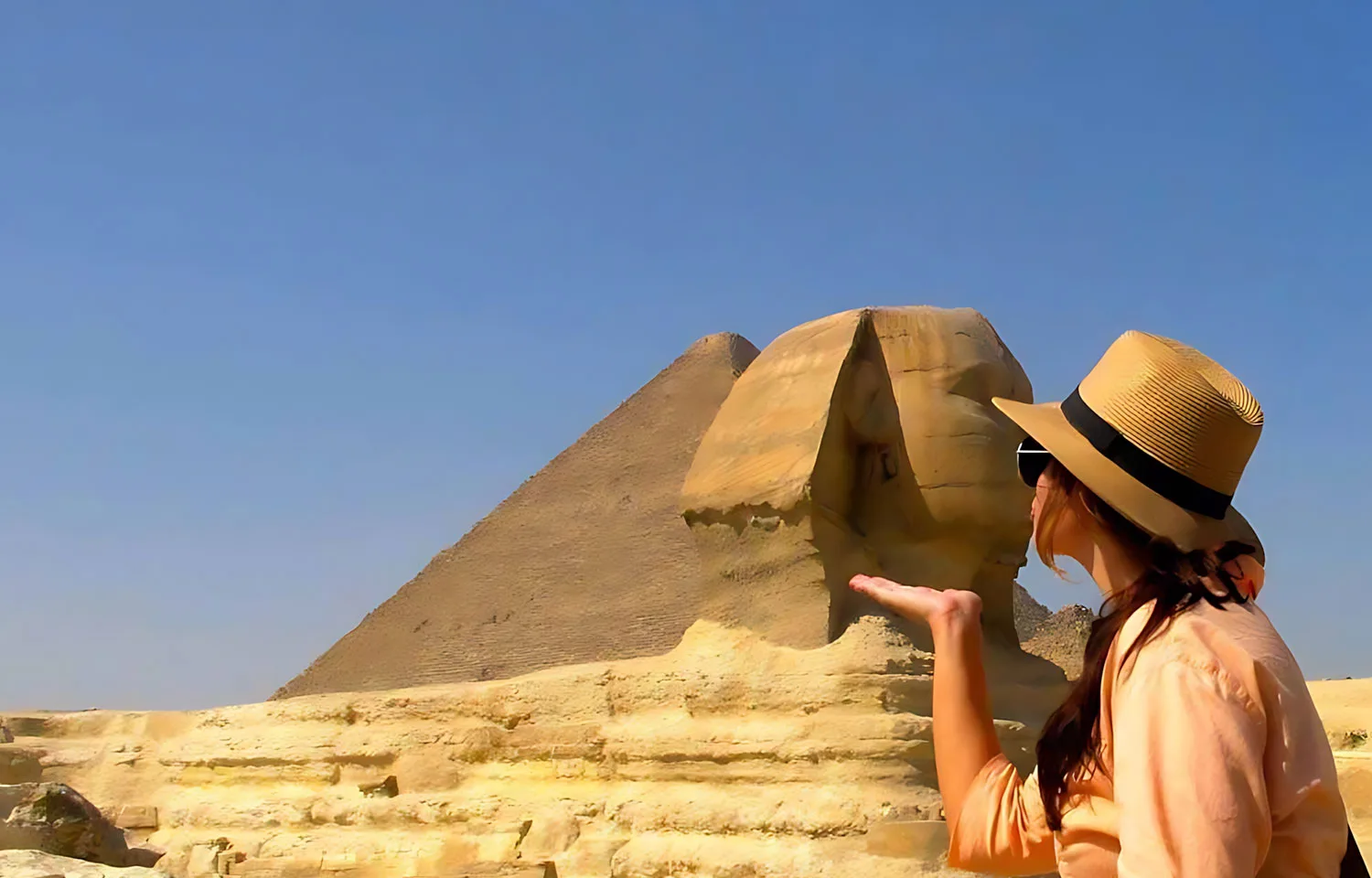 A traveler enjoying a Cairo pyramids half-day tour while posing playfully with the Great Sphinx