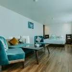 A spacious, modern Nile Cruise suite featuring a king-size bed in the background and a separate seating area with a sofa, two teal velvet armchairs, and a coffee table in the foreground.