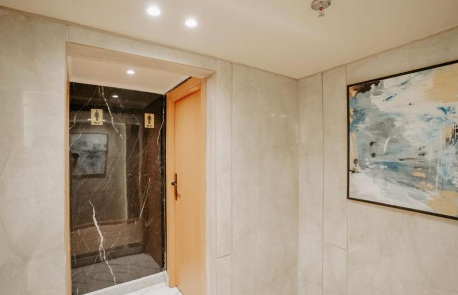 A contemporary hallway entrance to a public restroom area on a Nile Cruise, featuring light marble-look walls, a wooden door, and a black marble-look entrance with restroom icons.