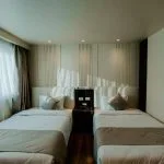 A contemporary twin cabin on a Nile Cruise with two single beds, dark wood flooring, and a vibrant, modern painting of a stylized Egyptian face on the wall.