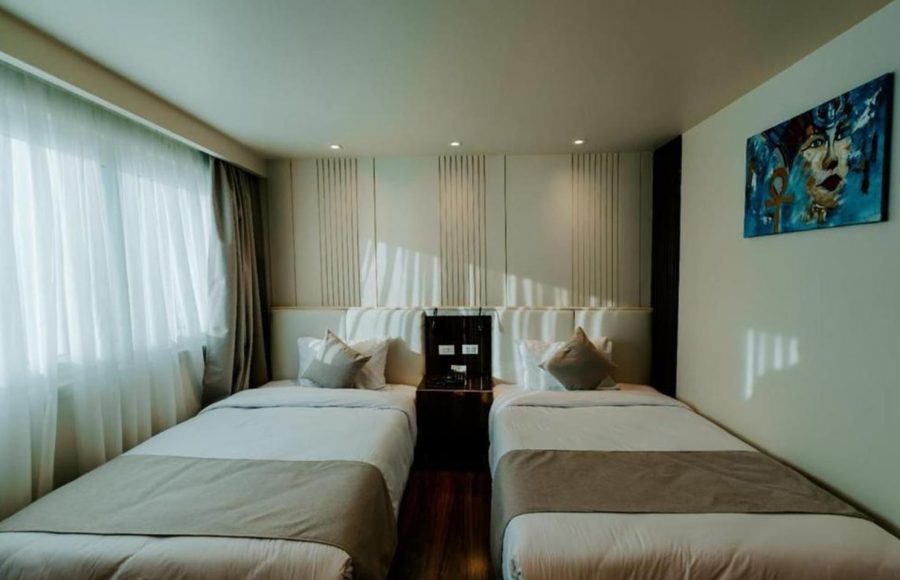 A contemporary twin cabin on a Nile Cruise with two single beds, dark wood flooring, and a vibrant, modern painting of a stylized Egyptian face on the wall.